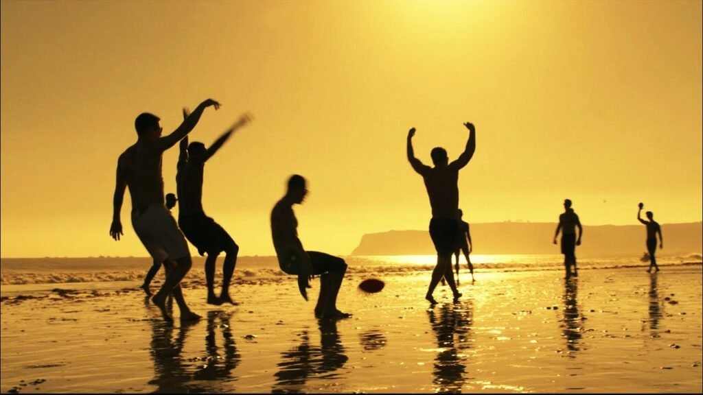 Personagens jogando futebol americano na praia em cena do filme Top Gun Maverick
