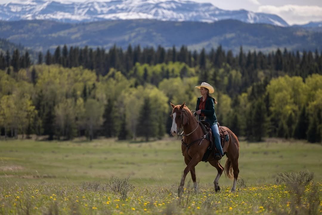 Amy cavalgando na 19ª temporada de Heartland, em uma paisagem aberta que mostra a vida no rancho e a conexão com os cavalos.