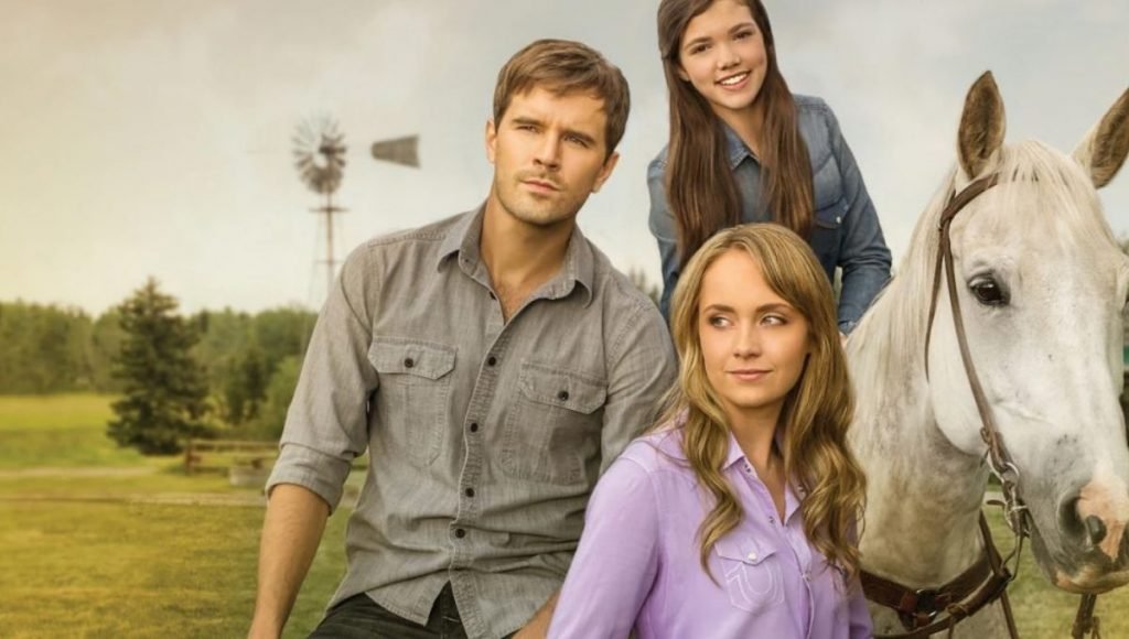 Cena da série Heartland com Amy, Ty e Georgie ao lado de um cavalo, destacando o clima acolhedor da história.