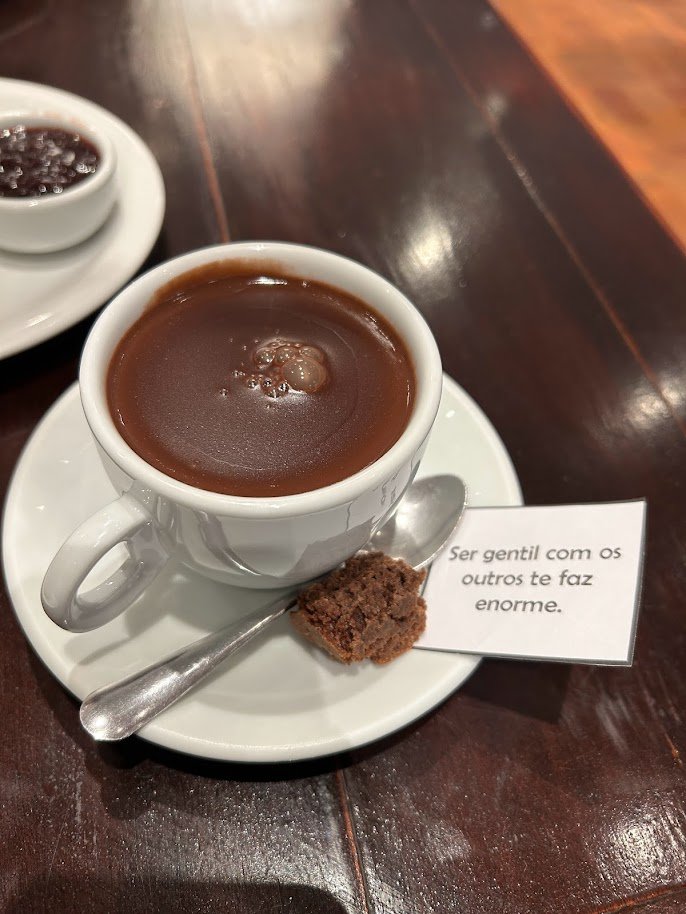 Chocolate quente na Sans Souci Café e Bistrô em Campos do Jordão, com uma mensagem sobre gentileza ao lado.