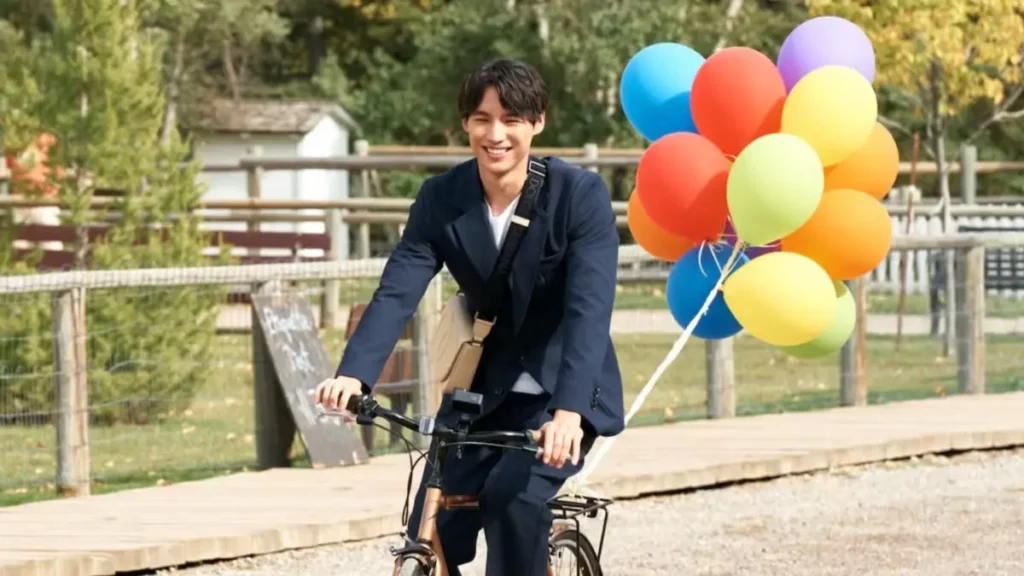 Hiro em cena de O Amor Pode Ser Traduzido?, dorama da Netflix, andando de bicicleta com balões coloridos.
