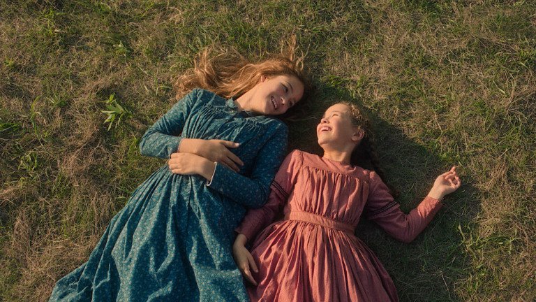 Laura e Mary deitadas na grama em uma cena de carinho entre irmãs em Uma Casa na Pradaria.