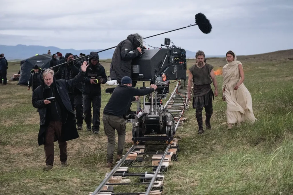 Bastidores das filmagens de A Odisseia, com equipe, atores e câmera IMAX montada sobre trilhos em uma locação externa.