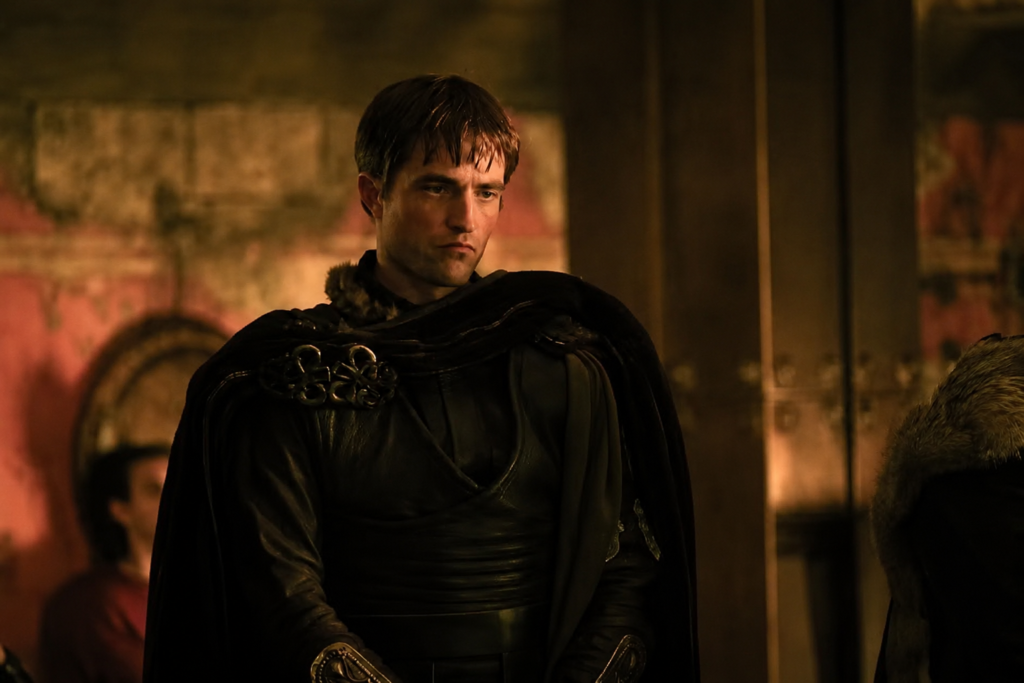 Robert Pattinson como Antínoo, usando traje escuro em cena do filme A Odisseia