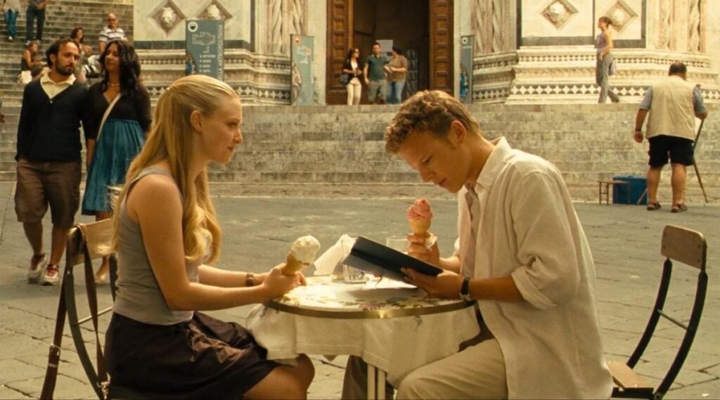 Cena de Cartas para Julieta com Sophie e Charlie sentados à mesa durante a viagem pela Itália, em um momento de aproximação entre os dois.