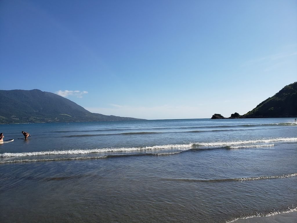 Praia de Barequeçaba, em São Sebastião, com mar calmo e montanhas ao fundo.