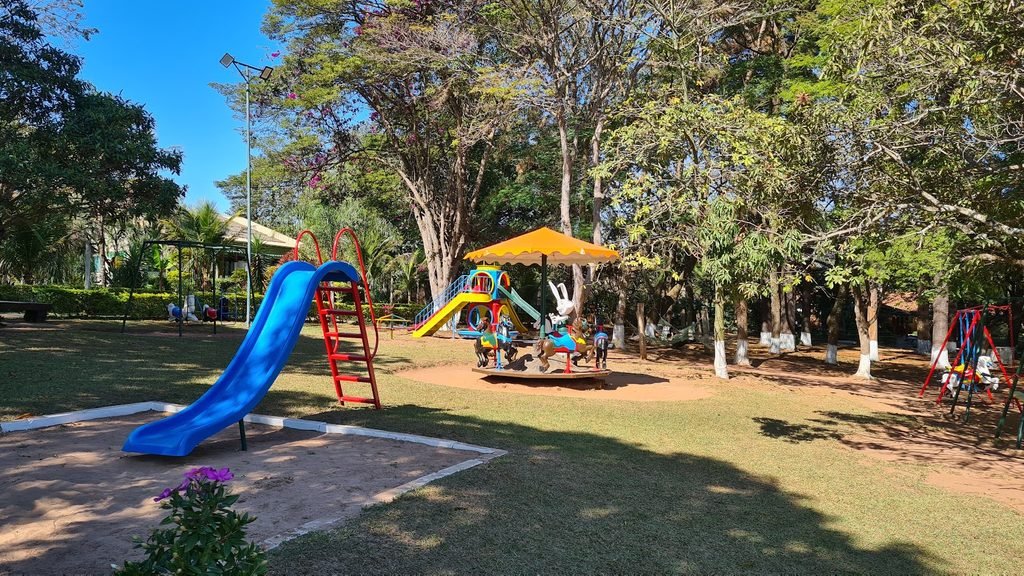 Parquinho infantil ao ar livre no Brotas Eco Hotel Fazenda, com escorregador e brinquedos cercados por árvores.